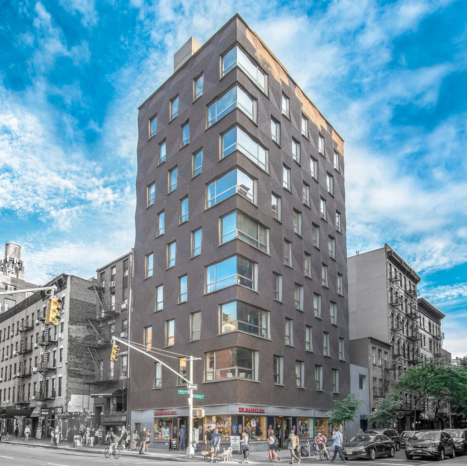 Dark brick mid-rise mixed-use building on a busy New York City corner with ground-floor retail.