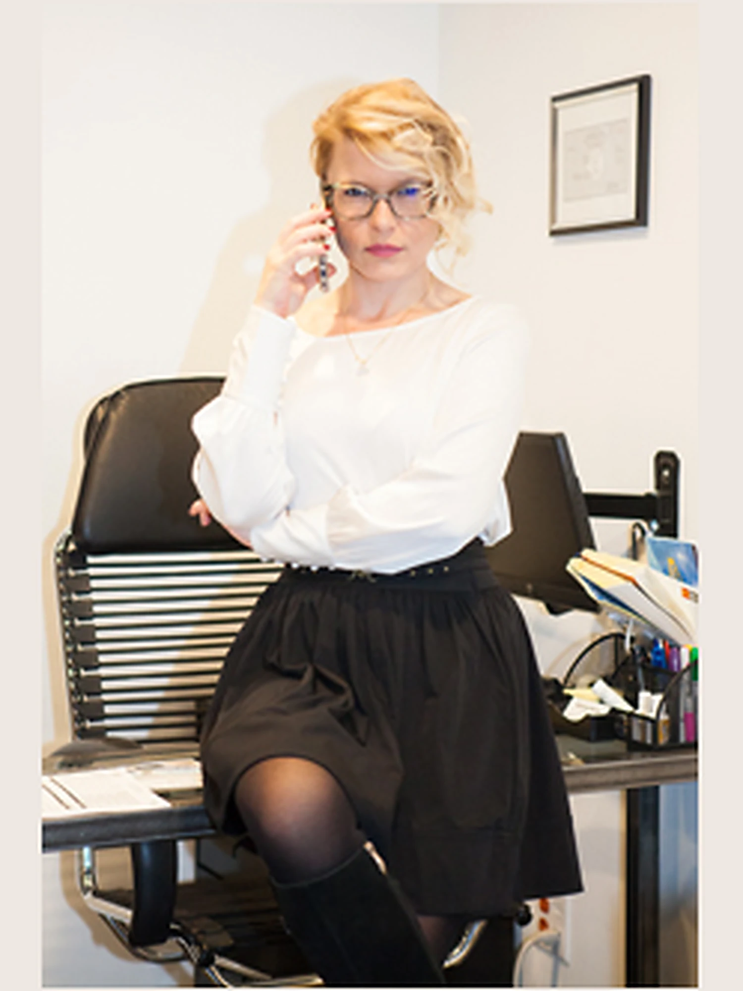 Founder and managing agent Katherine in stylish business attire seated on an office desk while speaking on a phone.