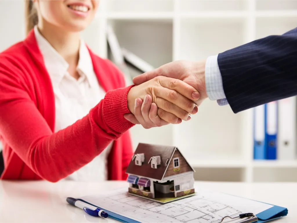 Business handshake above a model house and floor plan in a real estate office.