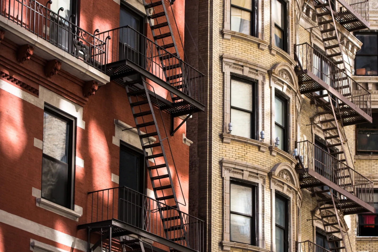 Close-up of NYC pre-war apartment building facades with exterior fire escapes along a street.